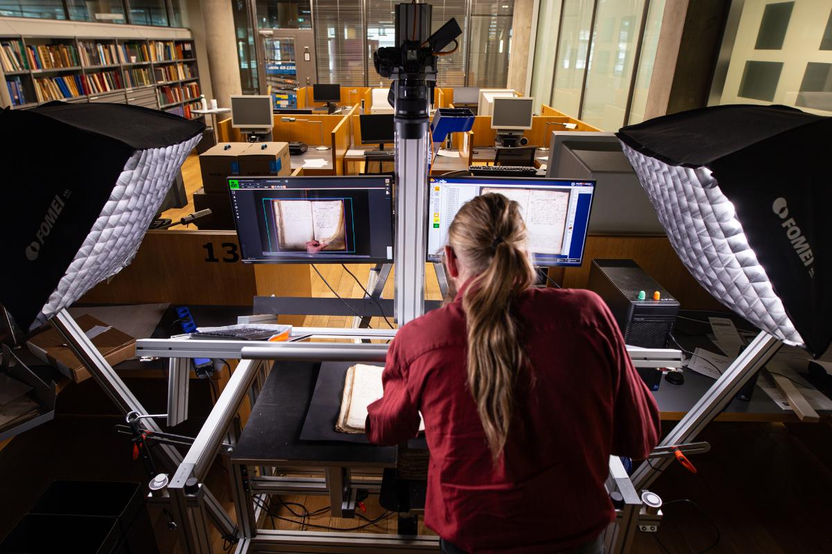 Kuvassa aineistoja digitoidaan Hämeenlinnassa. Kuvan keskellä on kuvauspöytä, jonka ääreellä aineistoa digitoi Kansallisarkiston työntekijä.