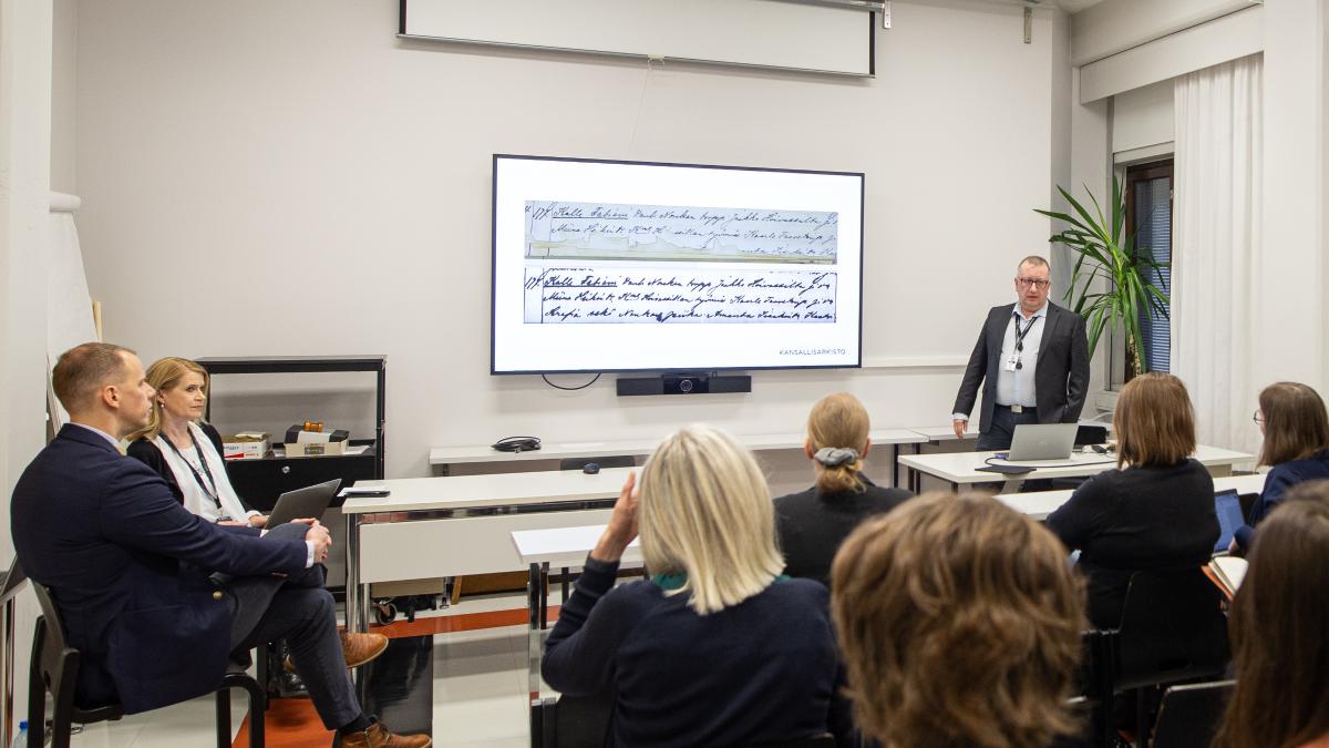 Kuvassa mies seisoo pienessä luentosalissa diaesityksen edessä.