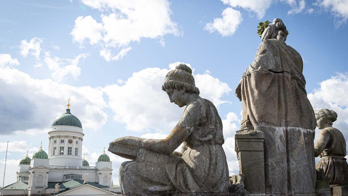 Kuvassa näkymä kansallisarkiston katolta, kolme antiikkityylistä patsasta Helsingin tuomiokirkon siluettia vasten.