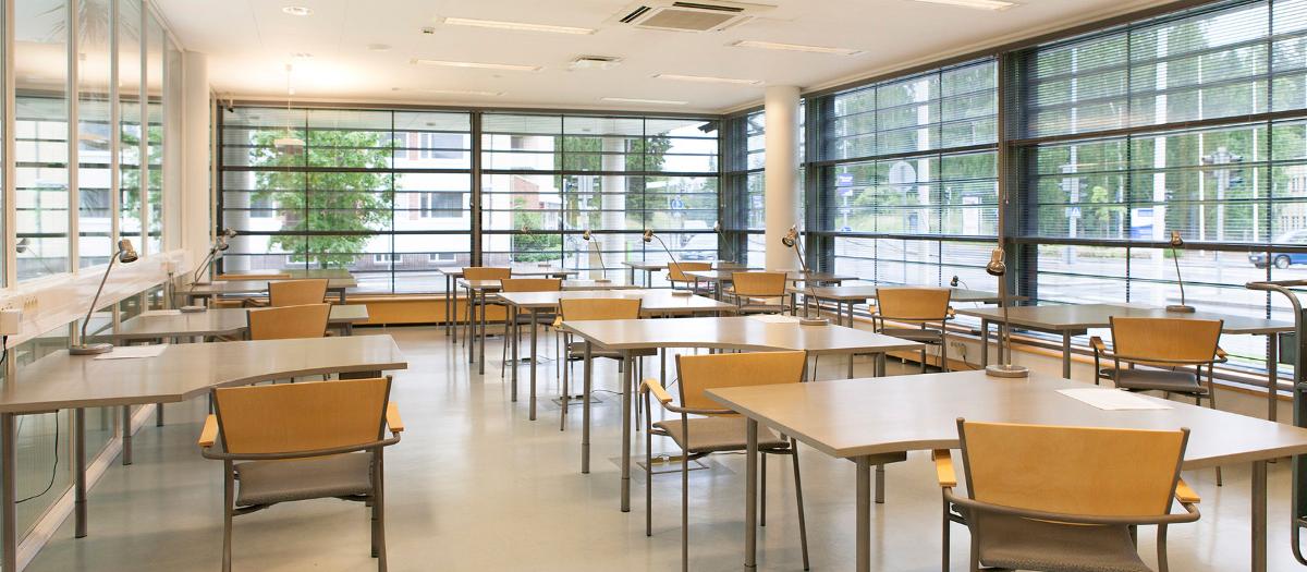 Kuvassa valoisa tutkijasali, jossa on useita pöytiä ja tuoleja ja suuret ikkunat.
